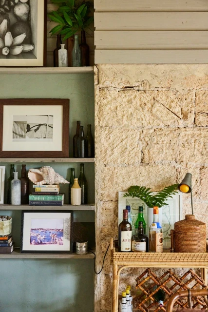 Interior featuring a stone accent wall with a wooden shelving unit displaying bottles, books, and decorative objects in soft lighting.
