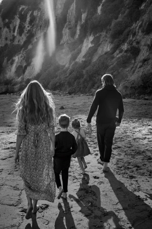 Family of four walking away on a sandy beach near a waterfall, captured in monochrome by Cheyenne Ellis.