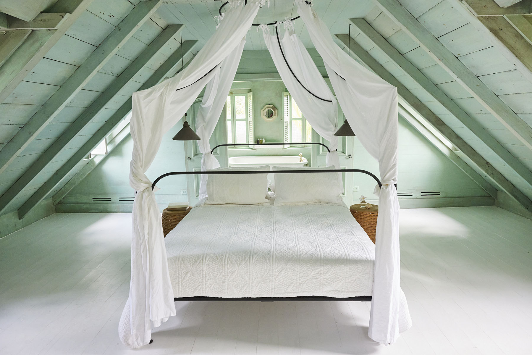 Interior shot of a canopy bed in an attic bedroom with slanted ceilings and pastel colors creating a serene and inviting atmosphere.
