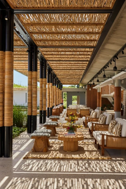Open-air lounge area features cushioned seating, rattan tables and light filtering through a bamboo canopy, creating dappled shadows.