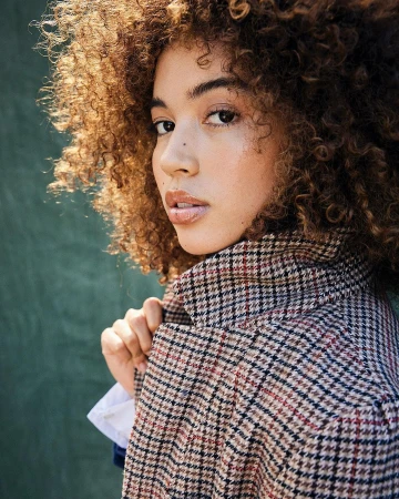 Portrait of a woman with voluminous curly brown hair wearing a patterned houndstooth coat, photographed by Cheyenne Ellis.