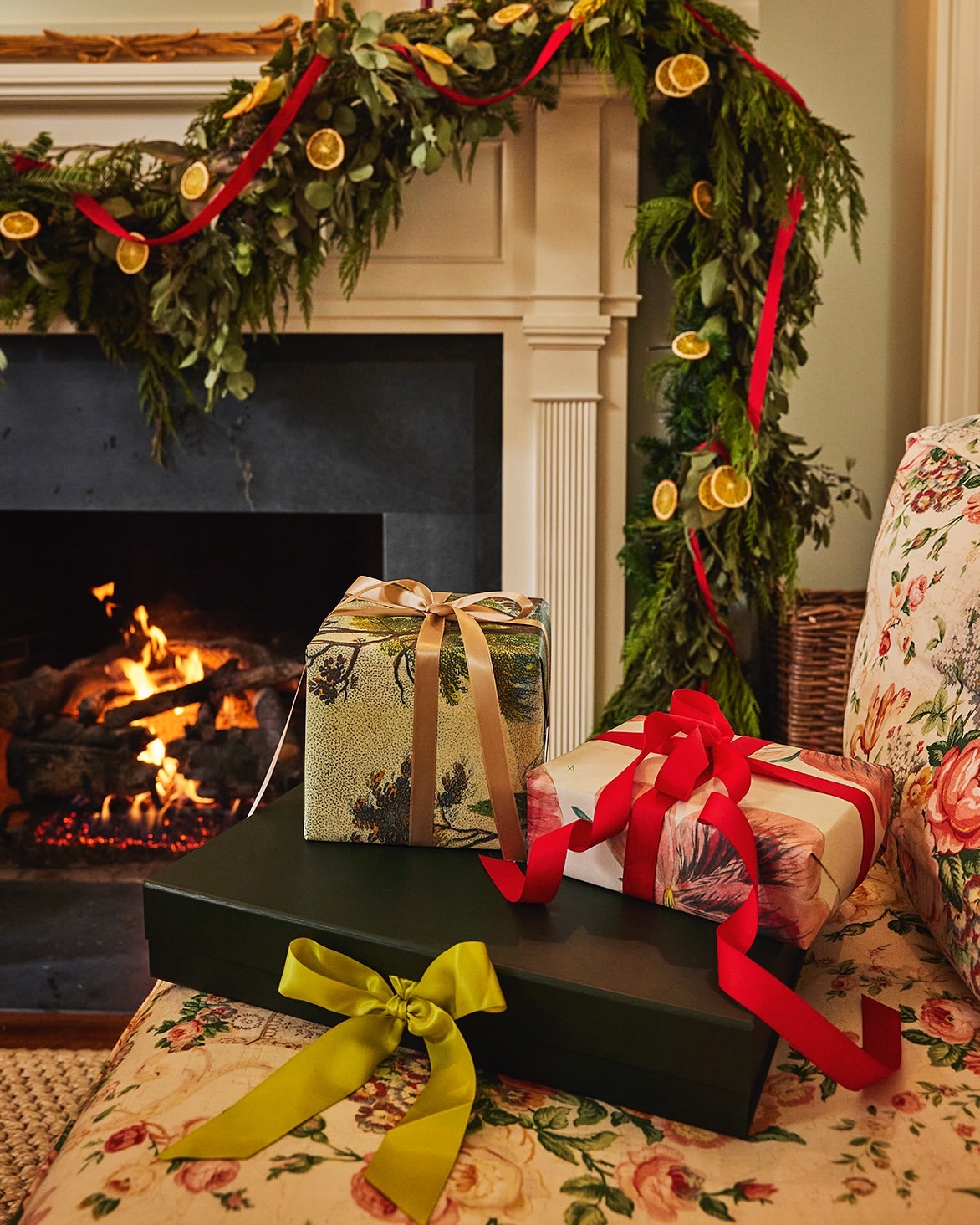 Festive holiday scene with stacked gift-wrapped presents adorned with ribbons, set against a backdrop of a fireplace with a garland.