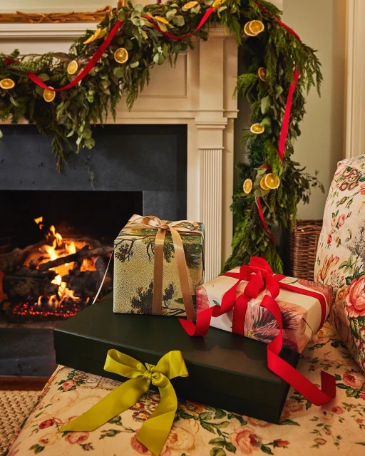 Festive holiday scene with stacked gift-wrapped presents adorned with ribbons, set against a backdrop of a fireplace with a garland.