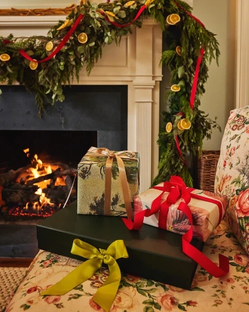 Festive holiday scene with stacked gift-wrapped presents adorned with ribbons, set against a backdrop of a fireplace with a garland.