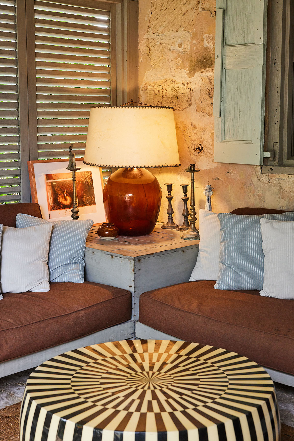 Cozy living room with armchairs, striped pillows, and a round coffee table, illuminated by a warm lamp and natural light.