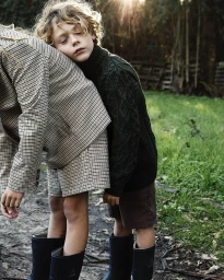 Child resting head on another person wearing a plaid blazer, outdoors near a grassy field