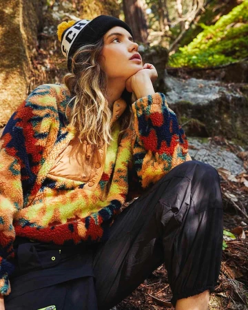 Young woman wearing a colourful patterned fleece pullover and black beanie outdoors among forest rocks.