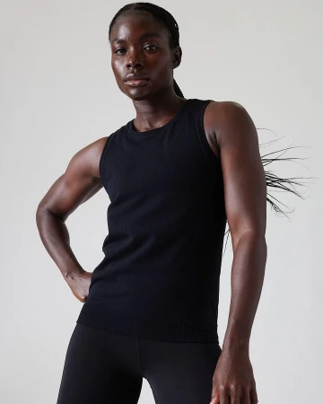 Black woman wearing a black ribbed tank top against a plain white background in portrait framing by Cheyenne Ellis