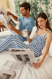 Man reading a newspaper and woman in striped pajamas holding a mug on a white bed