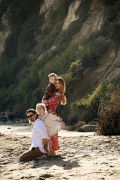 Family of four on a sandy beach below a rocky cliff, photographed by Cheyenne Ellis in natural light.