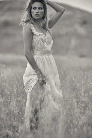 Black and white portrait of a woman standing in a grassy meadow wearing a lacy sundress