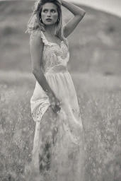 Black and white portrait of a woman standing in a grassy meadow wearing a lacy sundress