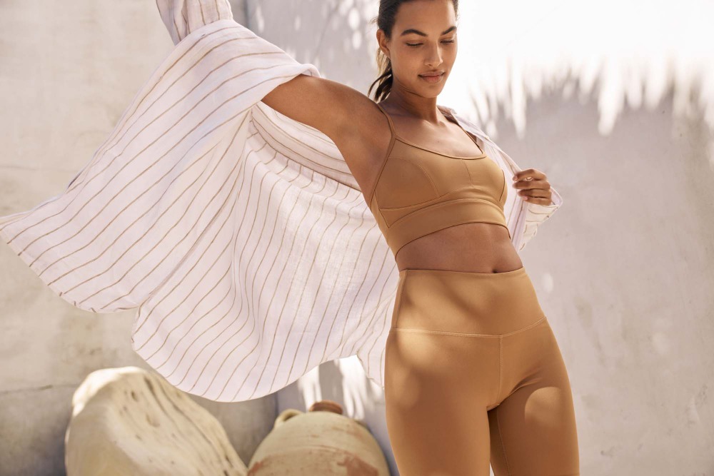 Woman in brown sports bra and leggings holding a striped button-down shirt outdoors