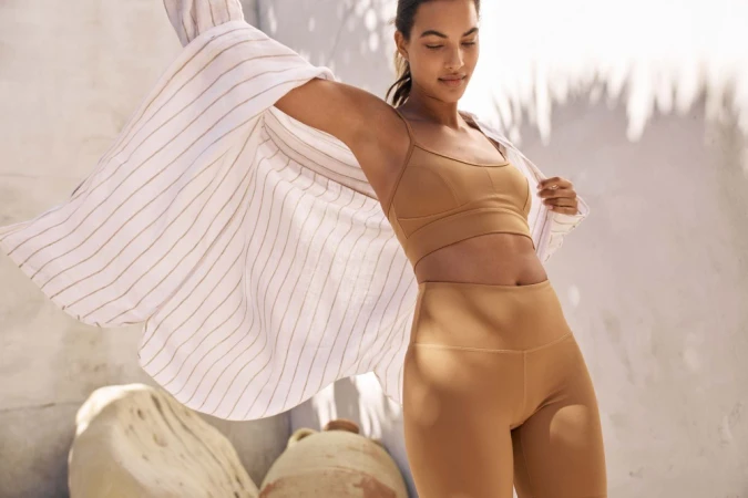 Woman in brown sports bra and leggings holding a striped button-down shirt outdoors