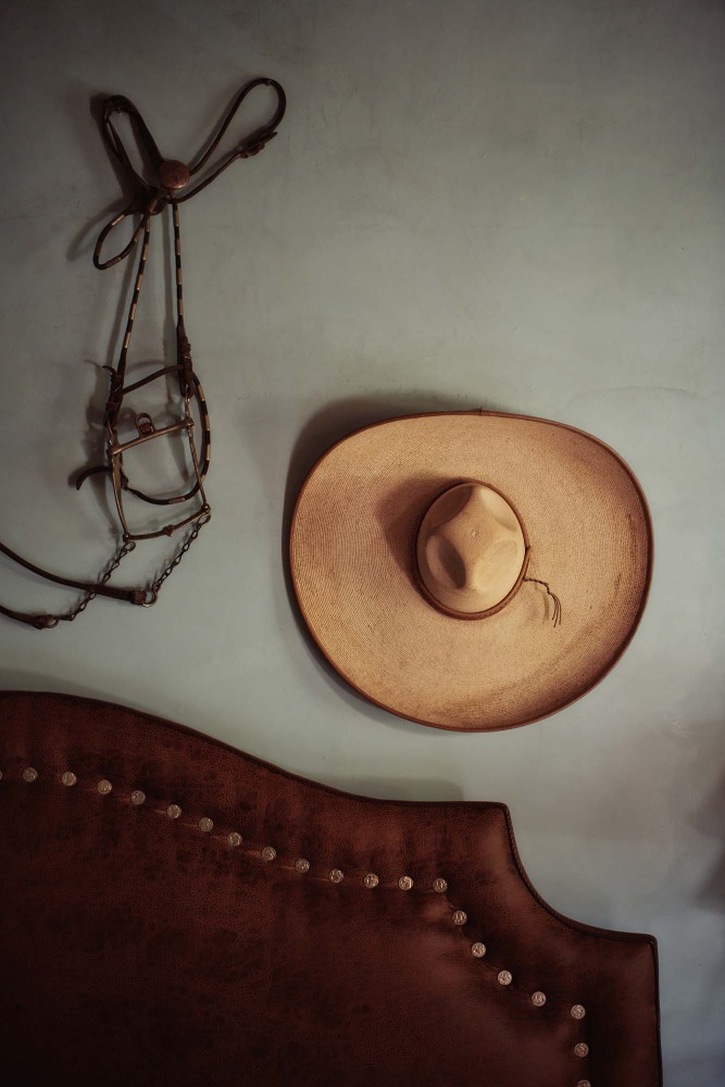A tan sombrero and decorative horse bridle hang on a light blue wall above a dark brown headboard with metallic studs.