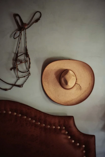 A tan sombrero and decorative horse bridle hang on a light blue wall above a dark brown headboard with metallic studs.