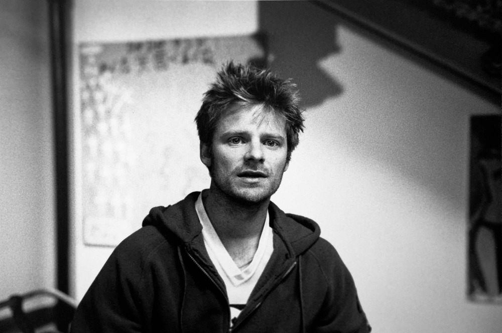 Black and white portrait of a man with tousled hair wearing a zip-up hoodie over a t-shirt by photographer Squire Fox