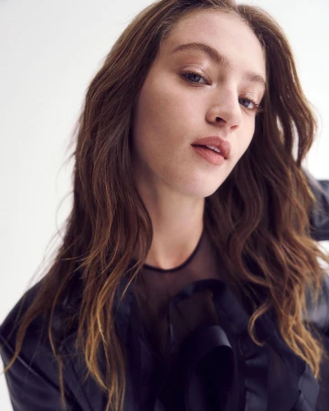 Close-up portrait of a woman with long wavy brown hair wearing a dark blouse against a white background
