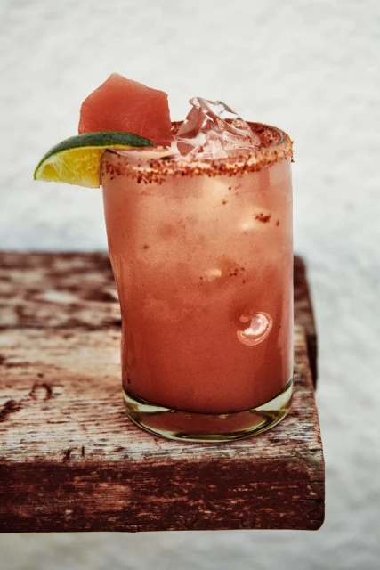 Refreshing watermelon margarita in a glass with a lime wedge and chili salt rim on a rustic wooden surface; cool, bright beverage shot.