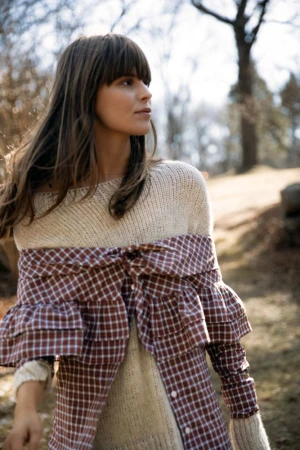 Woman in cream knit sweater and brown plaid shirt outdoors in a park by Squire Fox