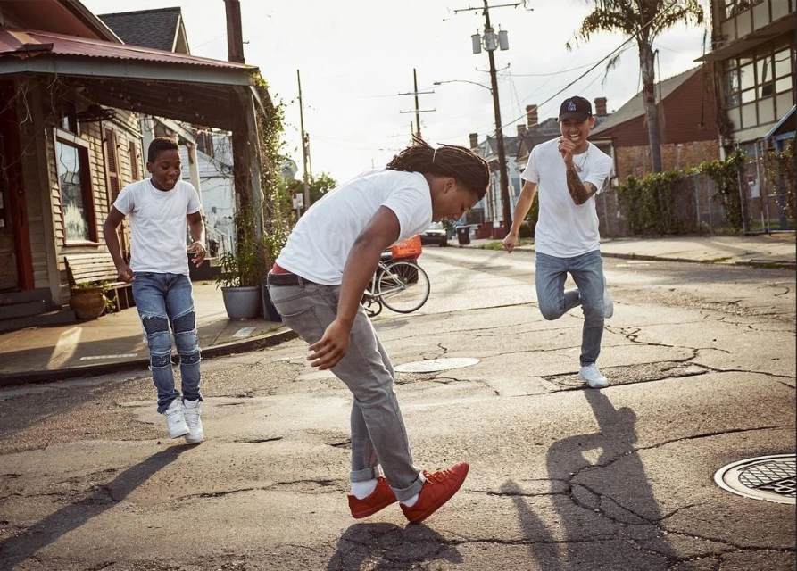 Three young men in casual wear are actively engaged in a game on a street in a residential area during daytime, capturing an active moment.