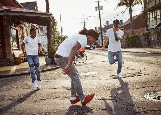 Three young men in casual wear are actively engaged in a game on a street in a residential area during daytime, capturing an active moment.