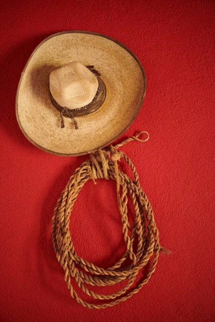A tan sombrero and rope hanging against a textured red wall create a rustic Southwestern or Mexican-themed decoration, indoors.