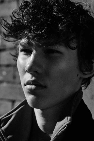 Close-up monochrome portrait of a young man with dark curly hair and a neutral expression by photographer Squire Fox.