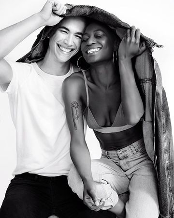Monochrome portrait of a smiling couple holding a denim jacket overhead in a photo studio. The black and white shot captures a joyful moment.