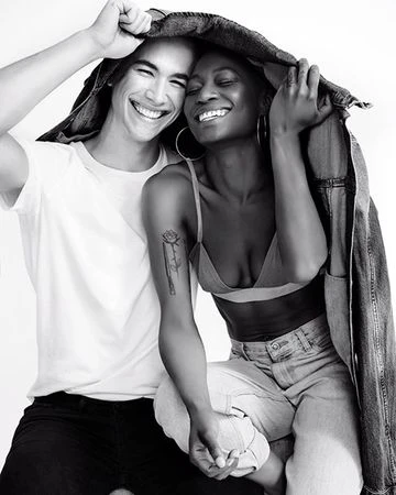 Monochrome portrait of a smiling couple holding a denim jacket overhead in a photo studio. The black and white shot captures a joyful moment.