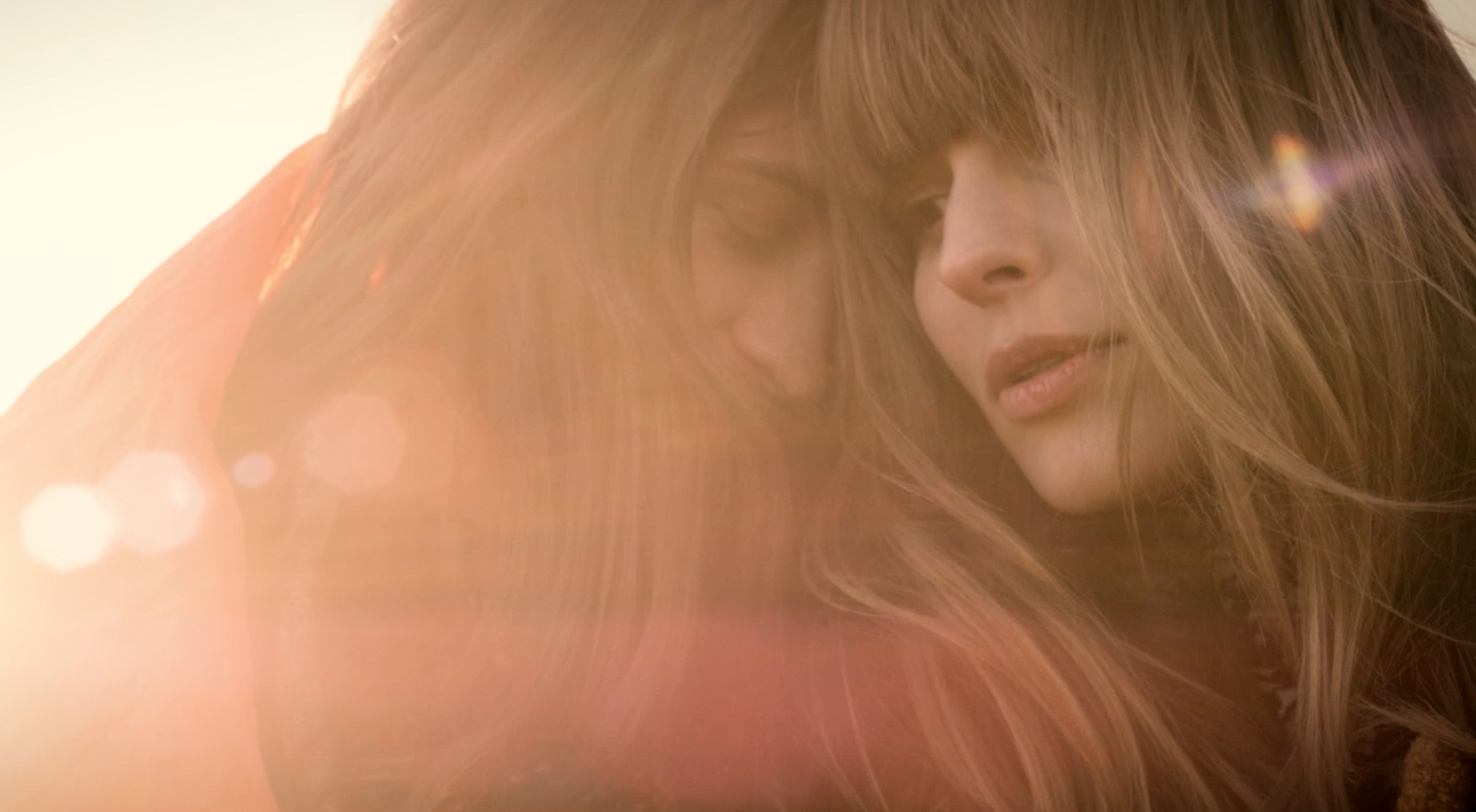Close-up of two women embracing, with long blonde hair, and soft, warm lighting creating an intimate and dreamy atmosphere.