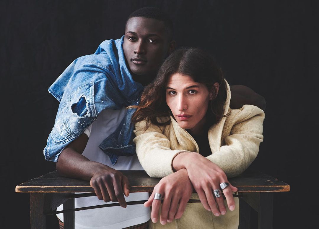 Two models posing behind a dark wooden desk against a plain black background, captured by Squire Fox.
