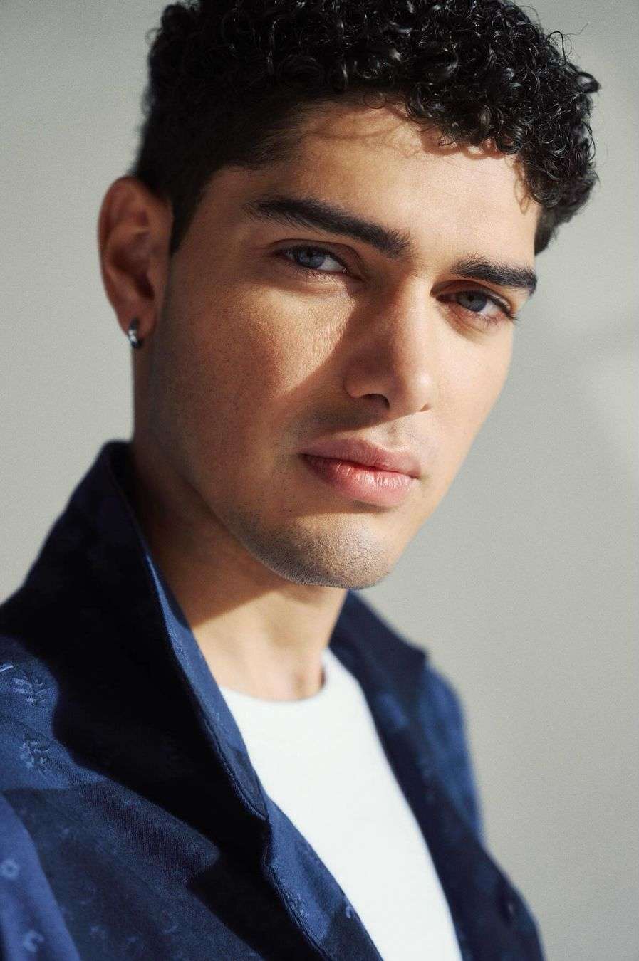 Close-up portrait of a young man with curly dark hair and blue shirt against a plain background photographed by Squire Fox.