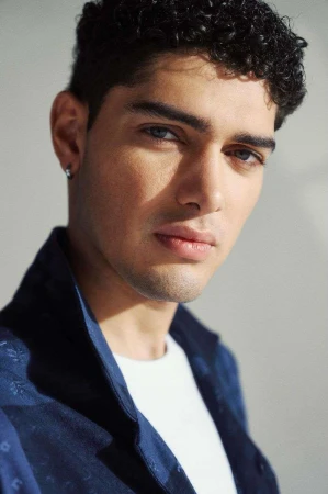 Close-up portrait of a young man with curly dark hair and blue shirt against a plain background photographed by Squire Fox.