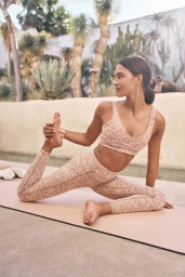 Woman in floral activewear holding her foot in a yoga pose outdoors near tropical foliage.