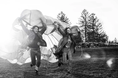 Black and white photograph of a man and a woman running outdoors while holding a large fabric parachute canopy.