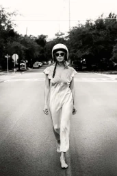 Woman walking barefoot down a middle of a street wearing a white slip dress, sunglasses, and a helmet, captured by Squire Fox.