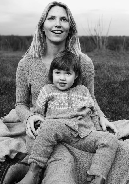 Black and white portrait of a mother and her young daughter sitting outside on a blanket, both wearing knitted sweaters.