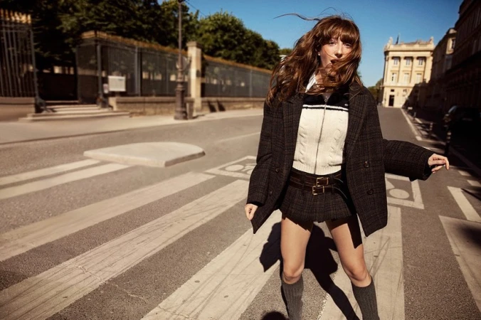 Woman with long brown hair in a plaid blazer and skirt standing on a sunny street