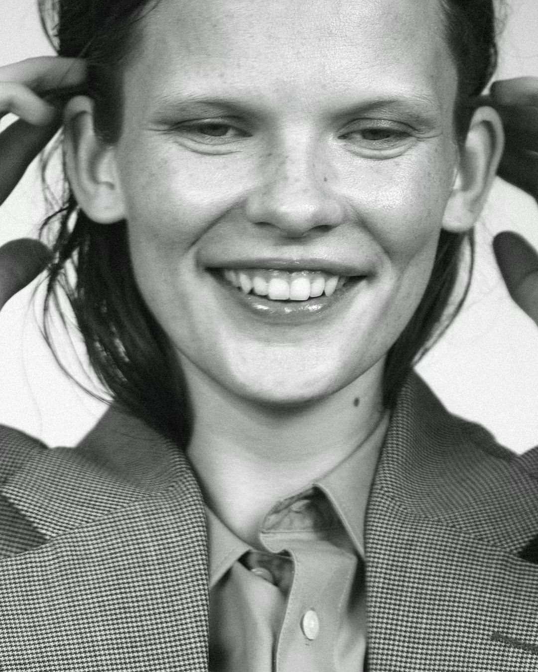 Close-up portrait of a smiling woman with short hair wearing a tailored houndstooth blazer and collared shirt.