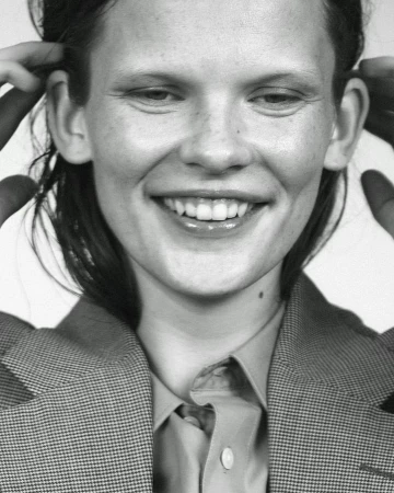 Close-up portrait of a smiling woman with short hair wearing a tailored houndstooth blazer and collared shirt.