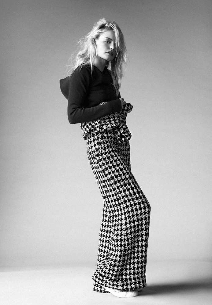A stylish young woman poses in a black hoodie and high-waisted, houndstooth wide-leg pants, looking confidently at the camera.