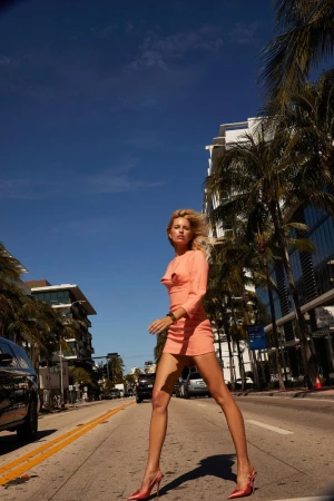 Model in a peach mini dress walking on a sunny city street lined with palm trees by Silja Magg
