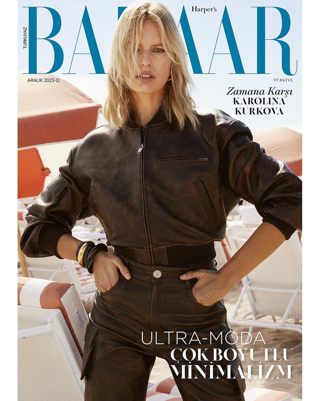 Harper's Bazaar cover featuring Karolina Kurkova in brown leather jacket and pants on a beach with sun umbrellas and lounge chairs.