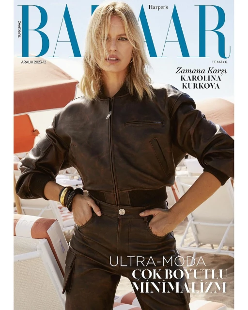 Harper's Bazaar cover featuring Karolina Kurkova in brown leather jacket and pants on a beach with sun umbrellas and lounge chairs.