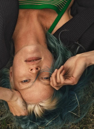 Close up portrait of a woman with teal hair and green top lying on grass, photographed by Silja Magg