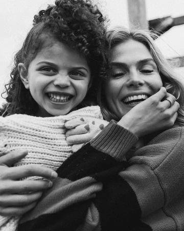 Black and white portrait of a smiling woman embracing a laughing child outdoors