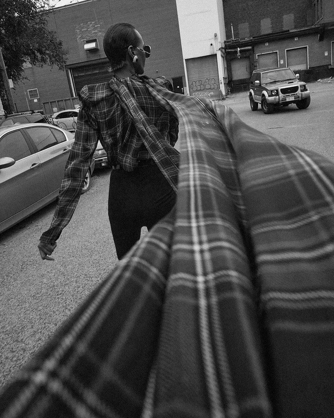 Model in dark plaid top with a long flowing scarf walking in an asphalt parking lot captured by Silja Magg