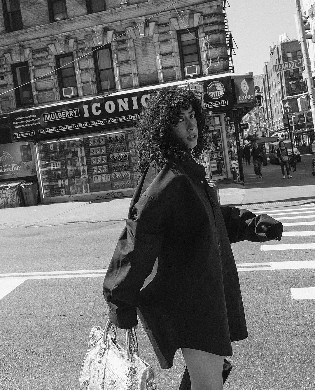 Woman with curly hair wearing an oversized shirt walking on a city street holding a handbag, photographed by Silja Magg.