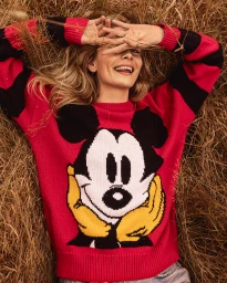 Smiling woman lying in dry grass wearing a red sweater with a large Mickey Mouse graphic